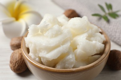 Shea butter in bowl, flower and nuts on white wooden table, closeup