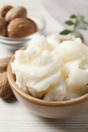 Shea butter in bowl and nuts on white wooden table, closeup