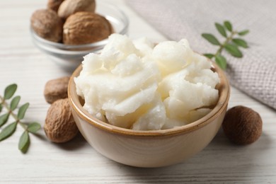 Shea butter in bowl and nuts on white wooden table, closeup