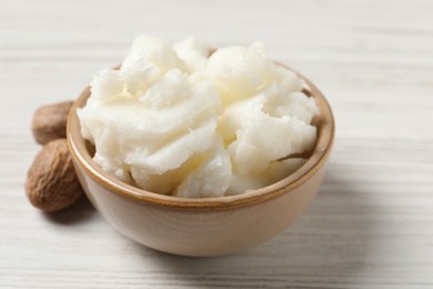 Shea butter in bowl and nuts on white wooden table, closeup