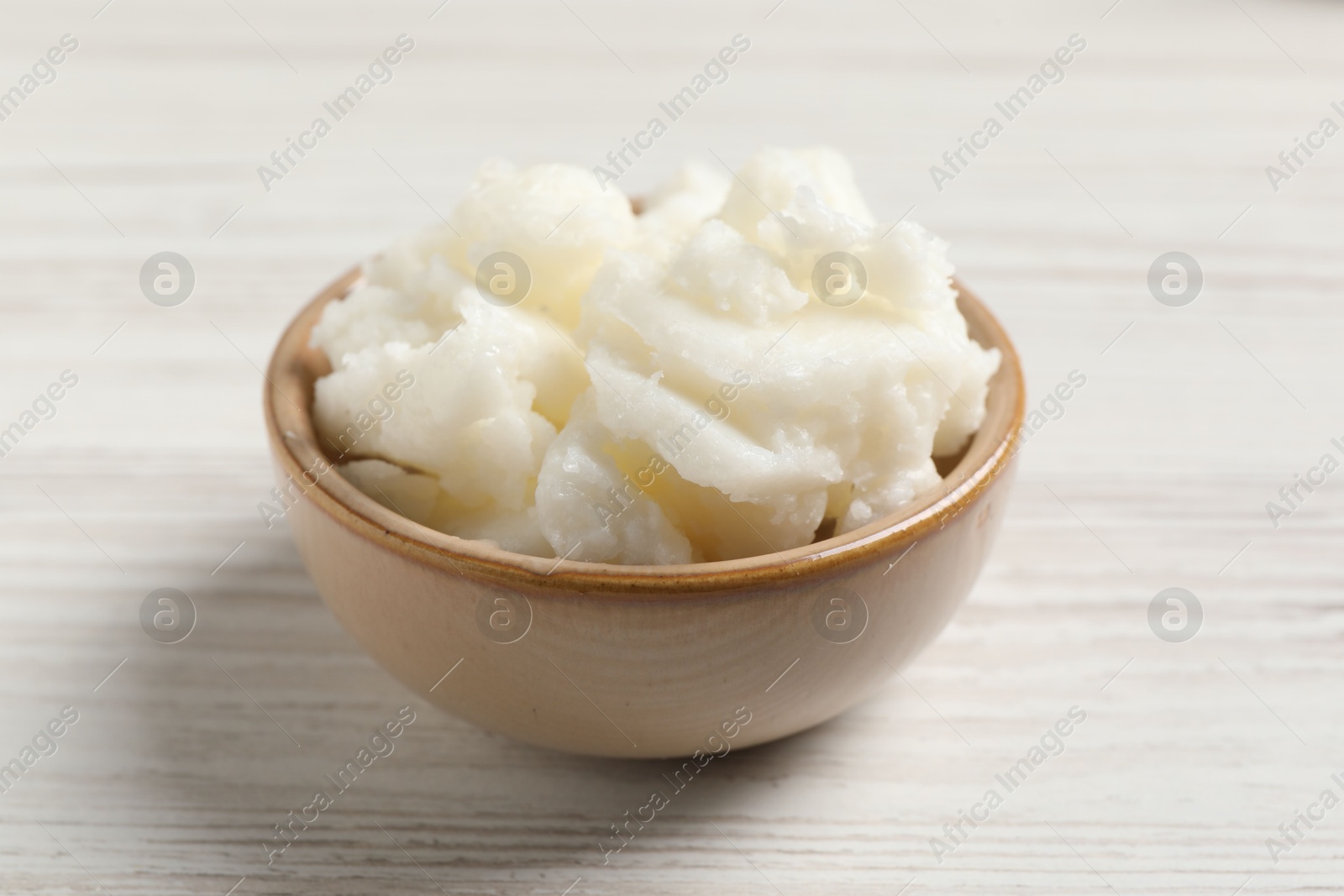 Photo of Shea butter in bowl on white wooden table, closeup