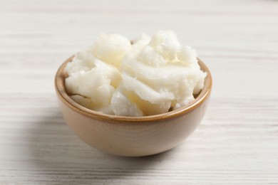 Photo of Shea butter in bowl on white wooden table, closeup