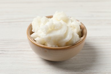 Shea butter in bowl on white wooden table, closeup