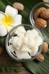 Photo of Shea butter in bowl, flower and nuts on wooden table, flat lay