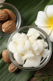 Shea butter in bowl, flower and nuts on wooden table, flat lay