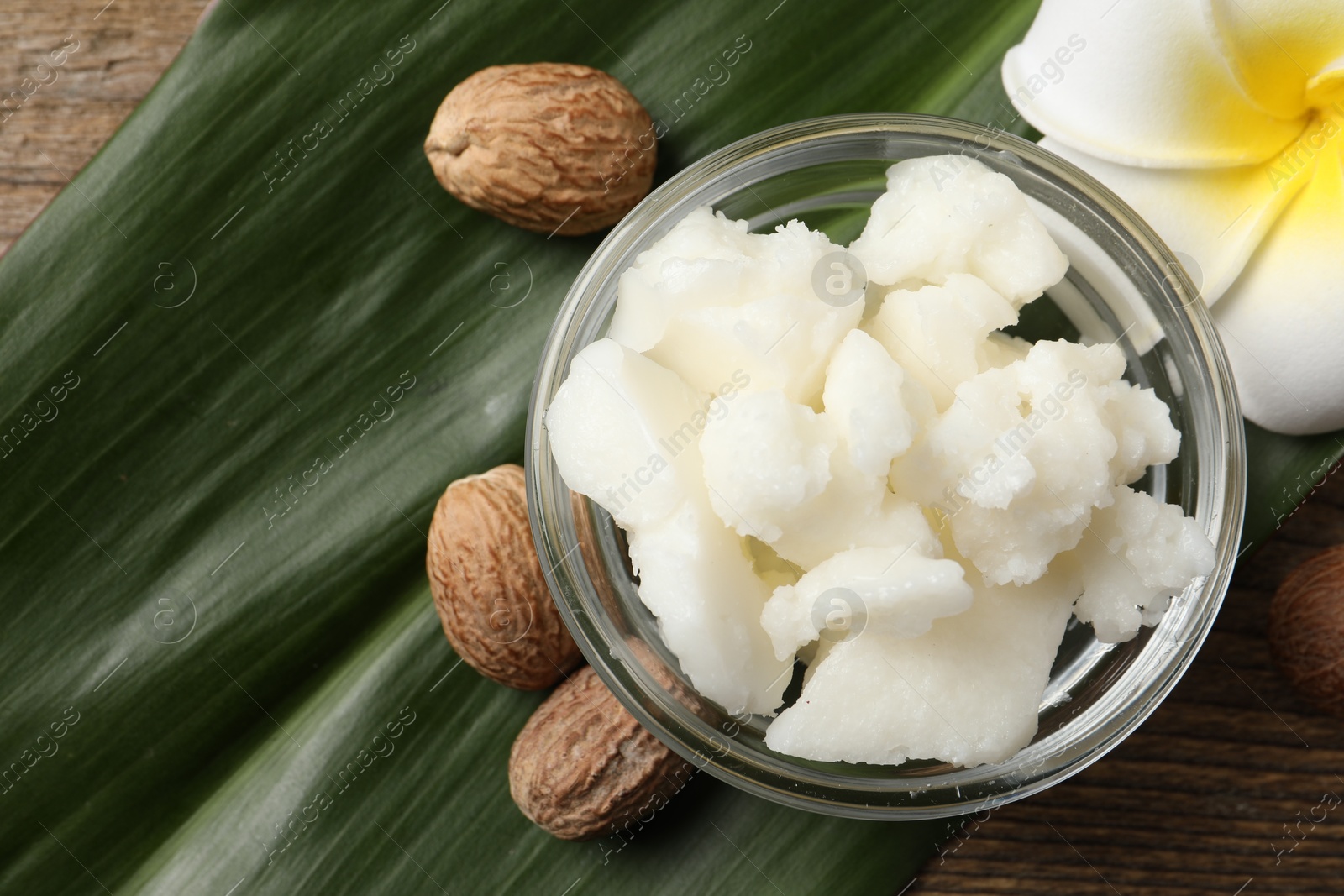 Photo of Shea butter in bowl, flower and nuts on wooden table, flat lay. Space for text