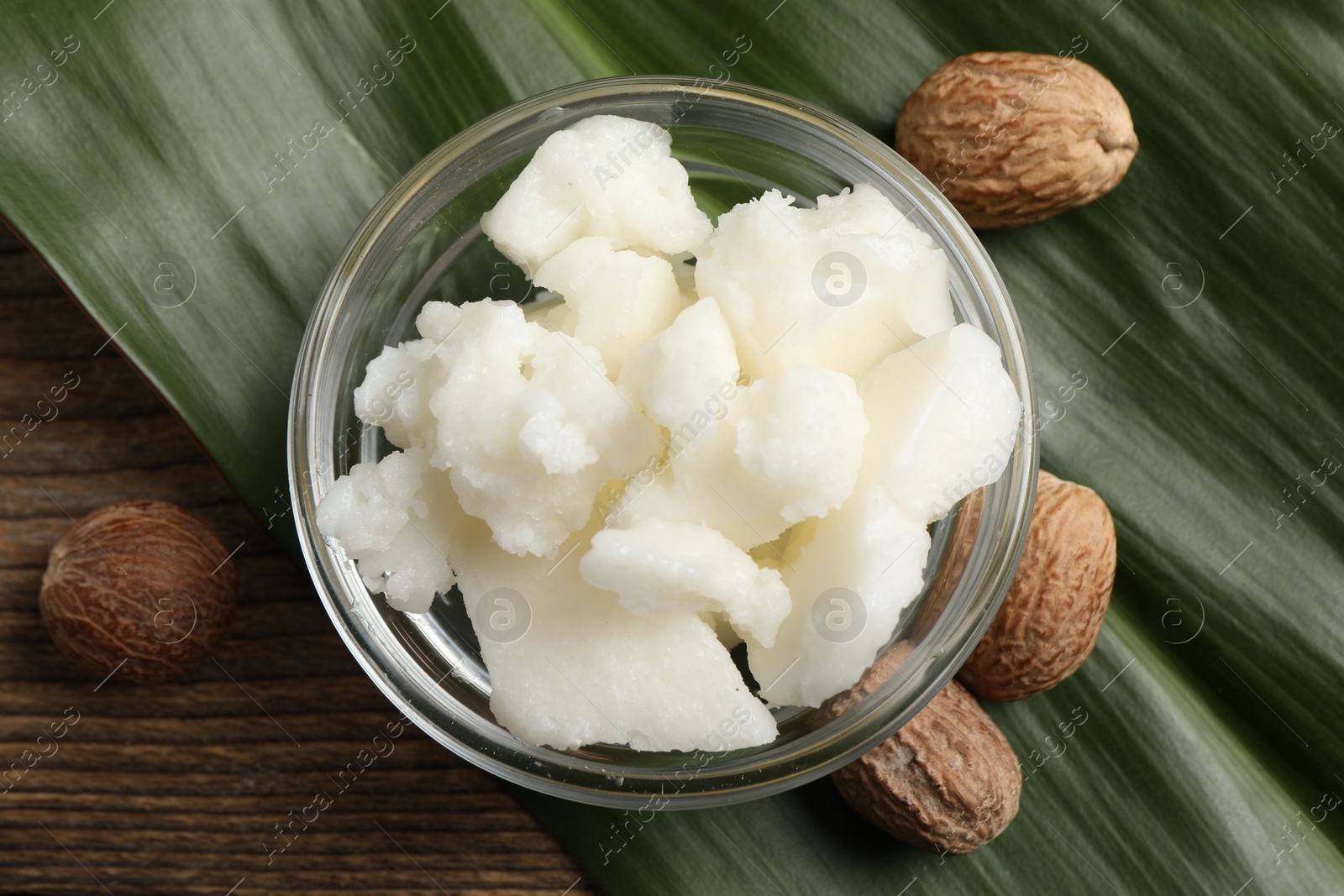 Photo of Shea butter in bowl and nuts on wooden table