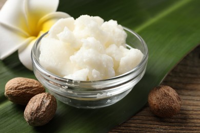 Photo of Shea butter in bowl, flower and nuts on wooden table, closeup