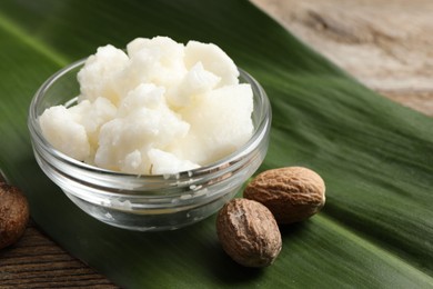 Shea butter in bowl and nuts on wooden table, closeup