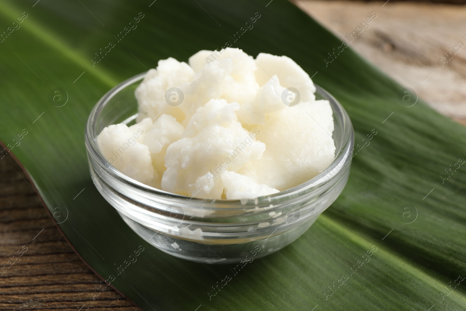 Photo of Shea butter in bowl and leaf wooden table, closeup