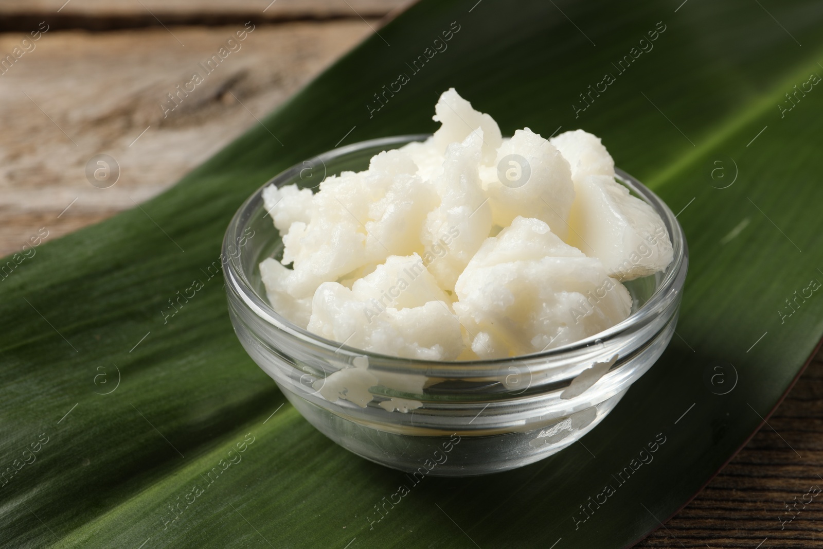 Photo of Shea butter in bowl and leaf wooden table, closeup