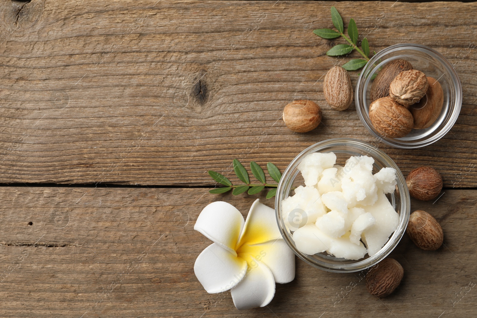 Photo of Shea butter in bowl, flower and nuts on wooden table, flat lay. Space for text