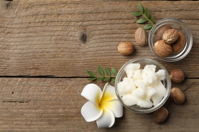 Photo of Shea butter in bowl, flower and nuts on wooden table, flat lay. Space for text