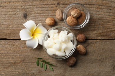 Photo of Shea butter in bowl, flower and nuts on wooden table, flat lay