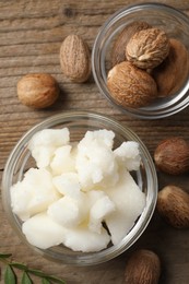 Photo of Shea butter in bowl and nuts on wooden table, flat lay