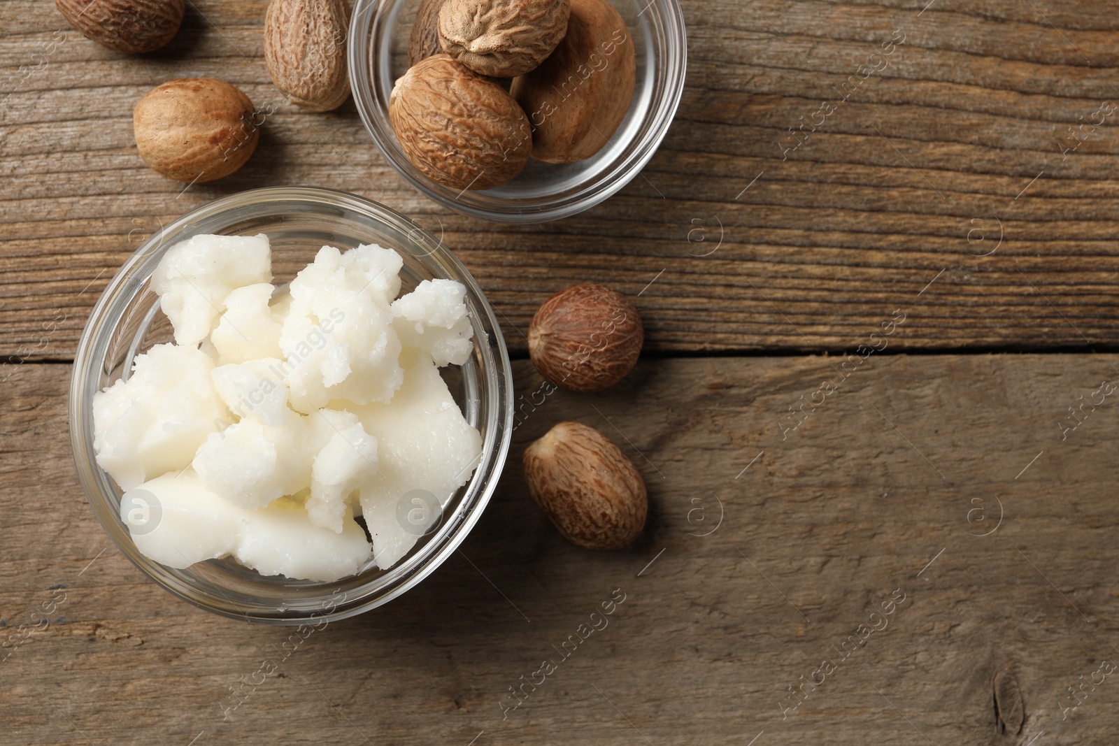 Photo of Shea butter in bowl and nuts on wooden table, flat lay. Space for text