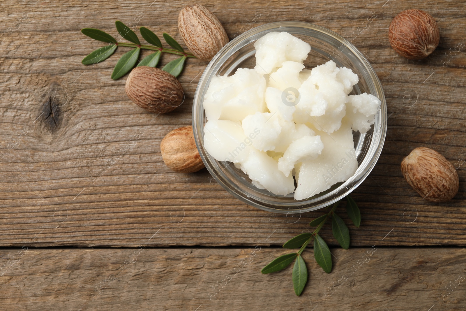 Photo of Shea butter in bowl and nuts on wooden table, flat lay. Space for text