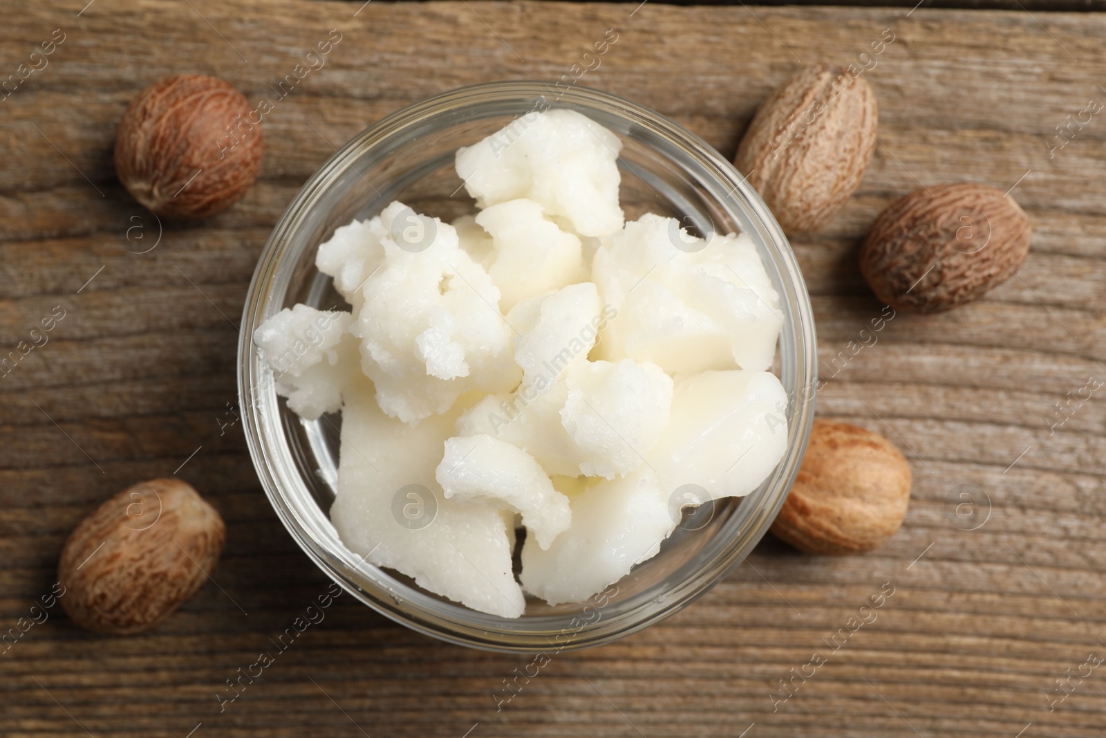 Photo of Shea butter in bowl and nuts on wooden table, flat lay