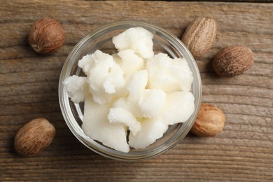 Shea butter in bowl and nuts on wooden table, flat lay