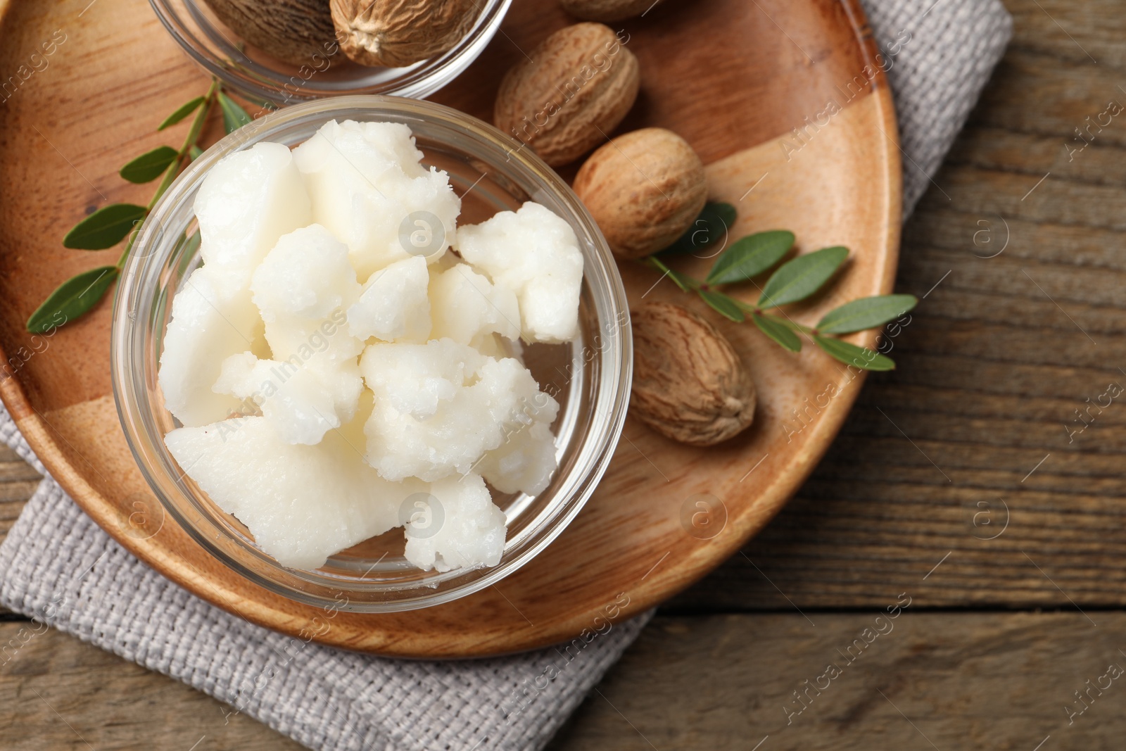 Photo of Shea butter in bowl and nuts on wooden table, top view