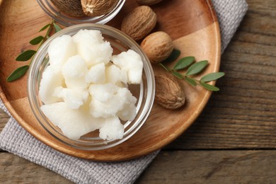 Shea butter in bowl and nuts on wooden table, top view