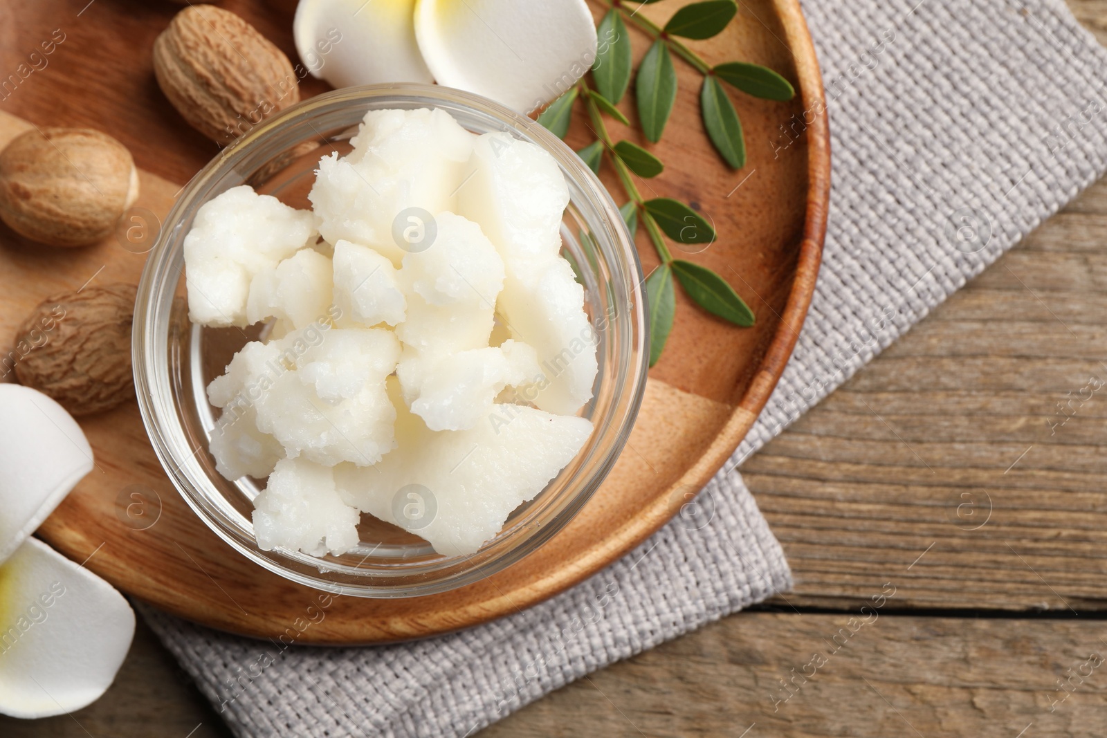 Photo of Shea butter in bowl, flowers and nuts on wooden table, top view. Space for text