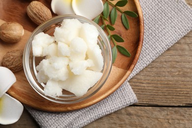 Photo of Shea butter in bowl, flowers and nuts on wooden table, top view. Space for text