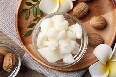 Shea butter in bowl, flowers and nuts on wooden table, flat lay