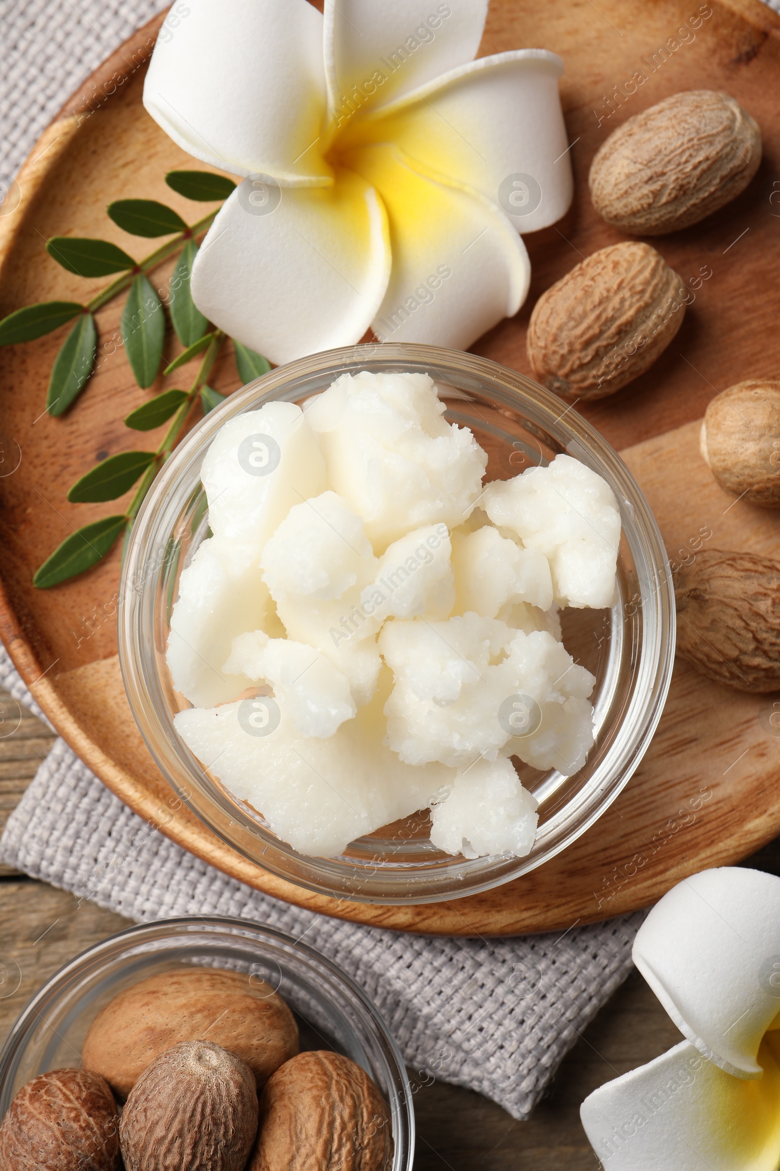 Photo of Shea butter in bowl, flowers and nuts on wooden table, flat lay