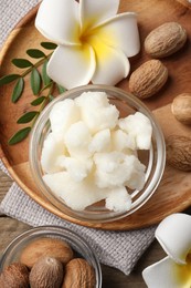 Shea butter in bowl, flowers and nuts on wooden table, flat lay