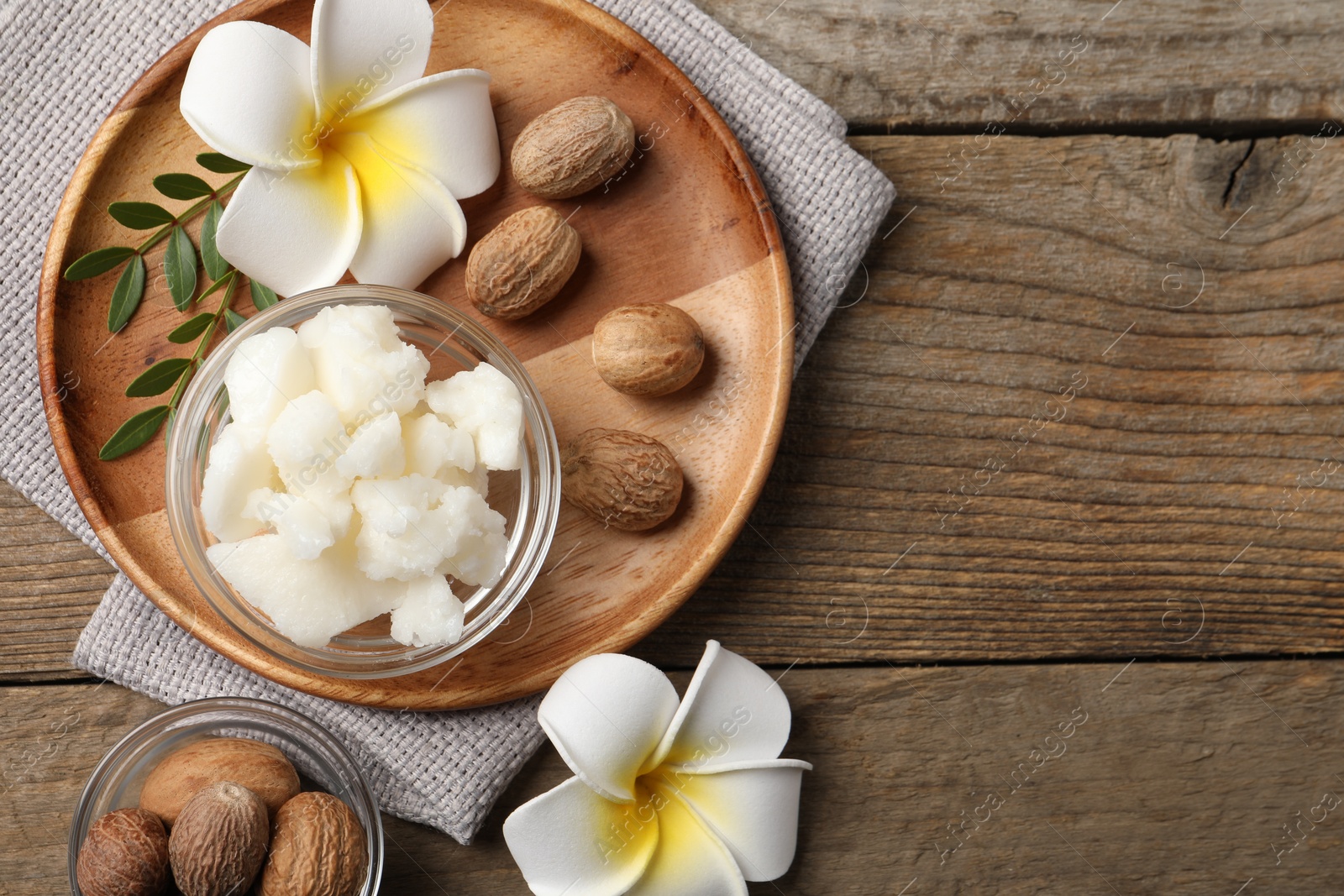 Photo of Shea butter in bowl, flowers and nuts on wooden table, flat lay. Space for text