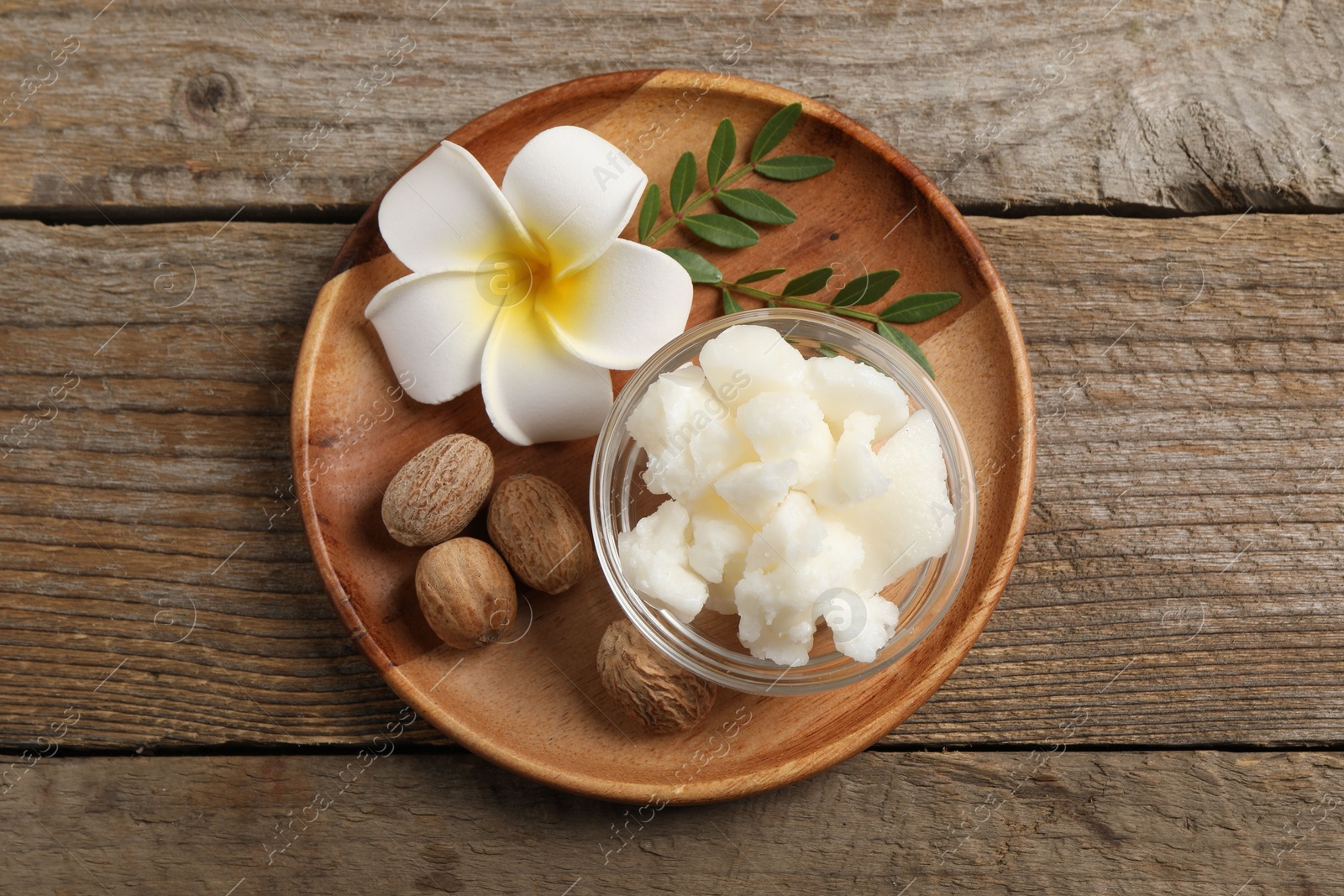 Photo of Shea butter in bowl, flower and nuts on wooden table, top view