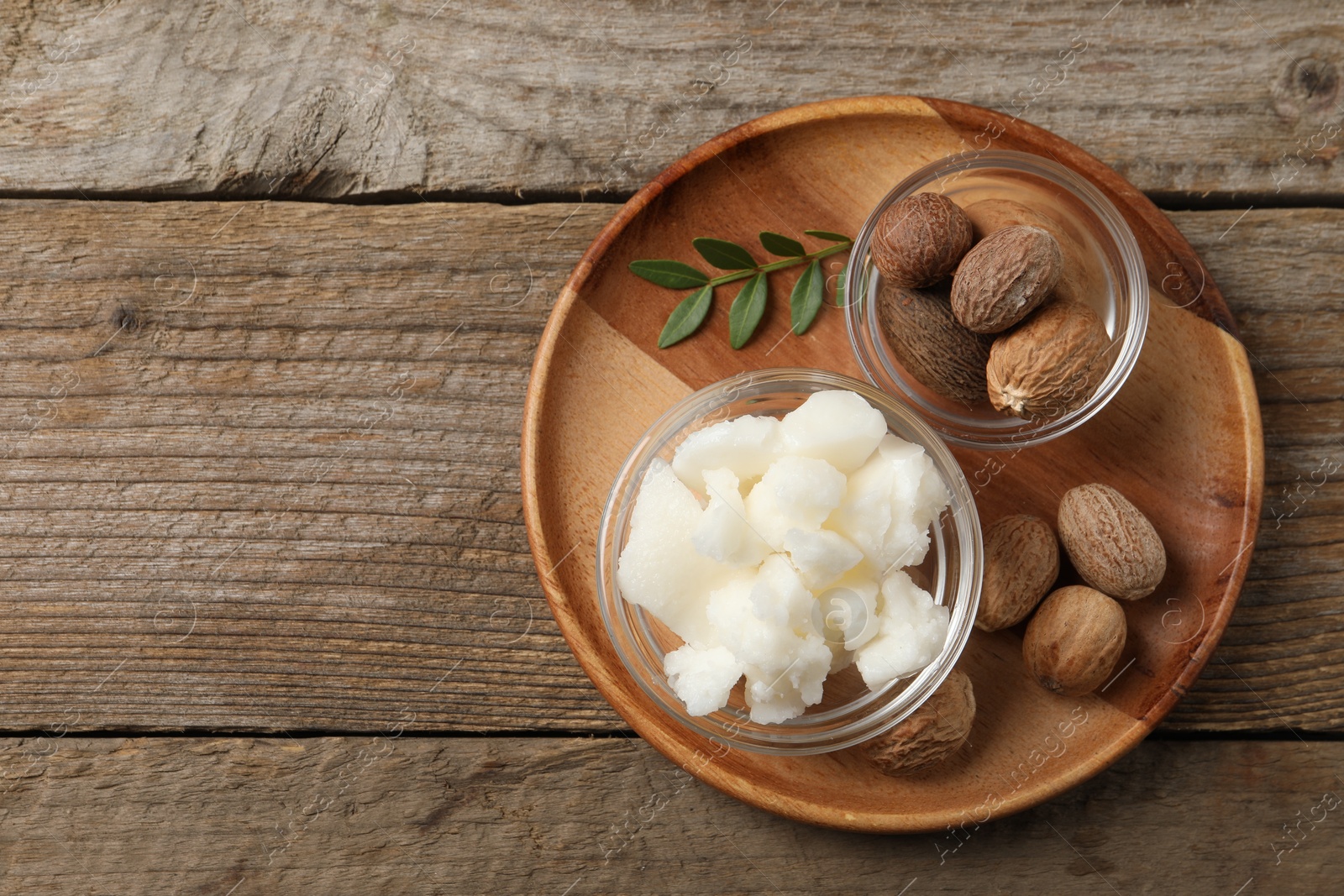 Photo of Shea butter in bowl and nuts on wooden table, top view. Space for text