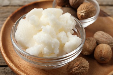 Photo of Shea butter in bowl and nuts on wooden table, closeup