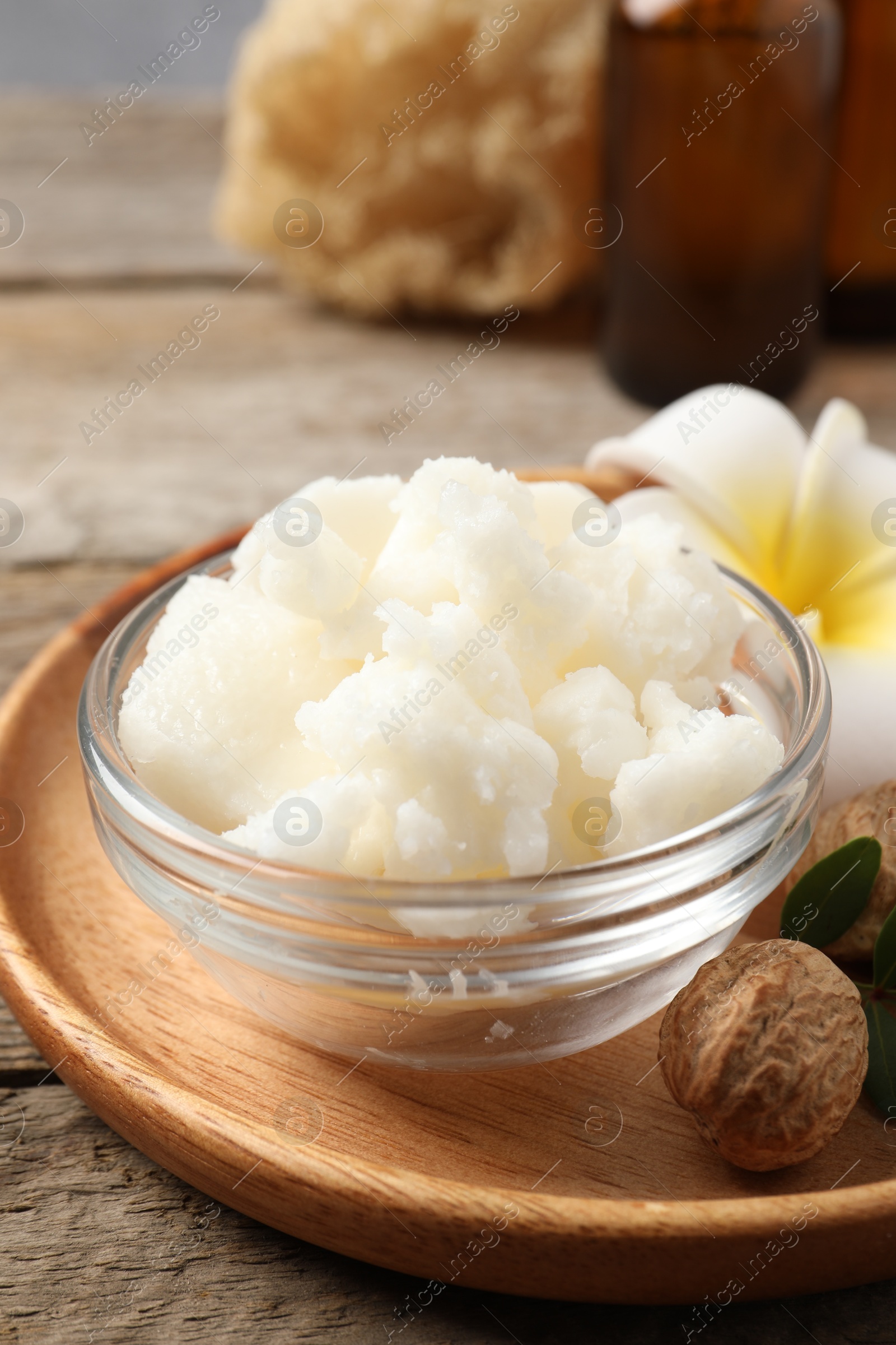 Photo of Shea butter in bowl, flower and nuts on wooden table, closeup