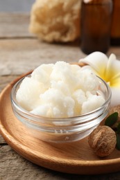 Shea butter in bowl, flower and nuts on wooden table, closeup