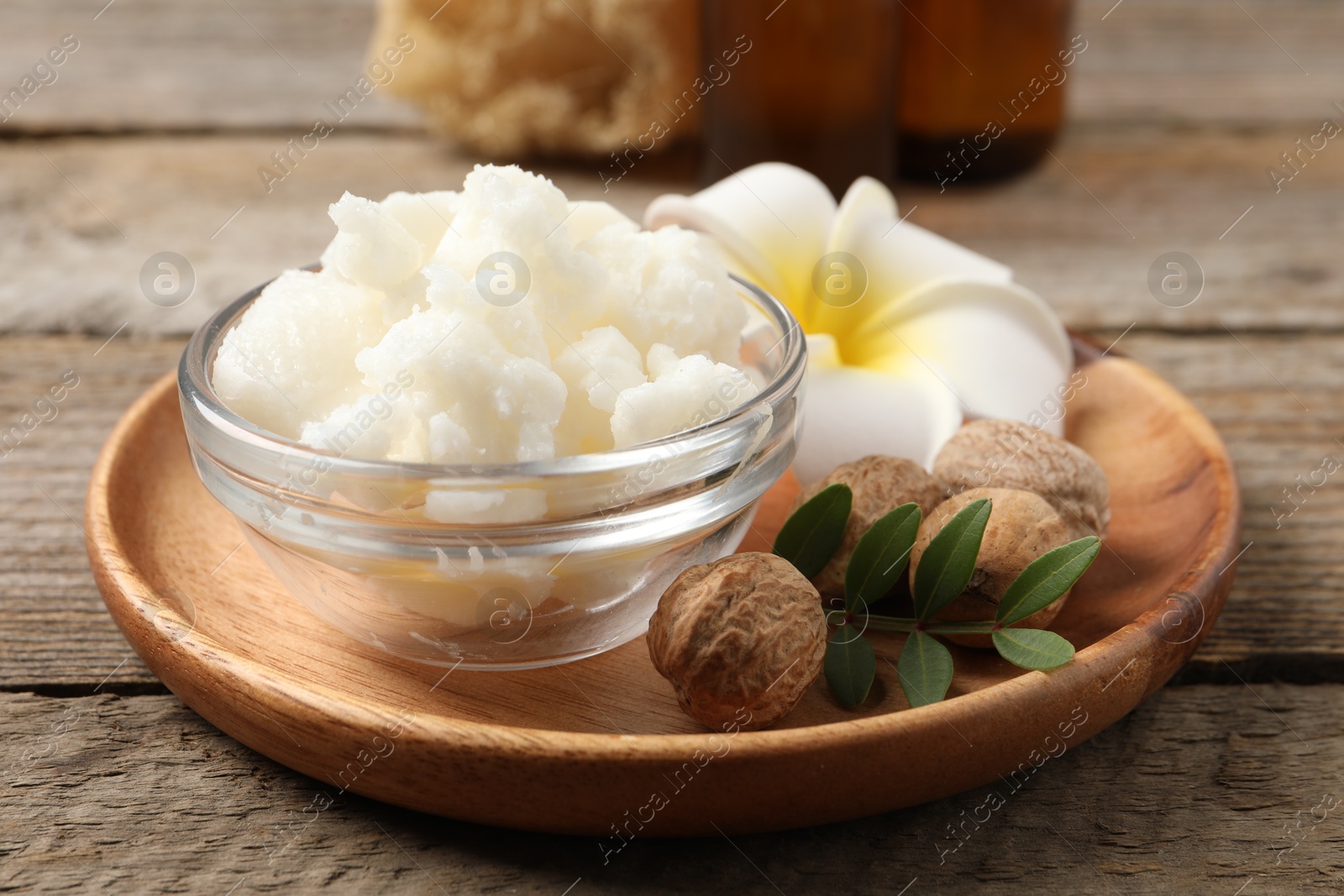 Photo of Shea butter in bowl, flower and nuts on wooden table, closeup