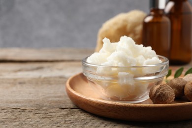 Shea butter in bowl and nuts on wooden table, closeup. Space for text