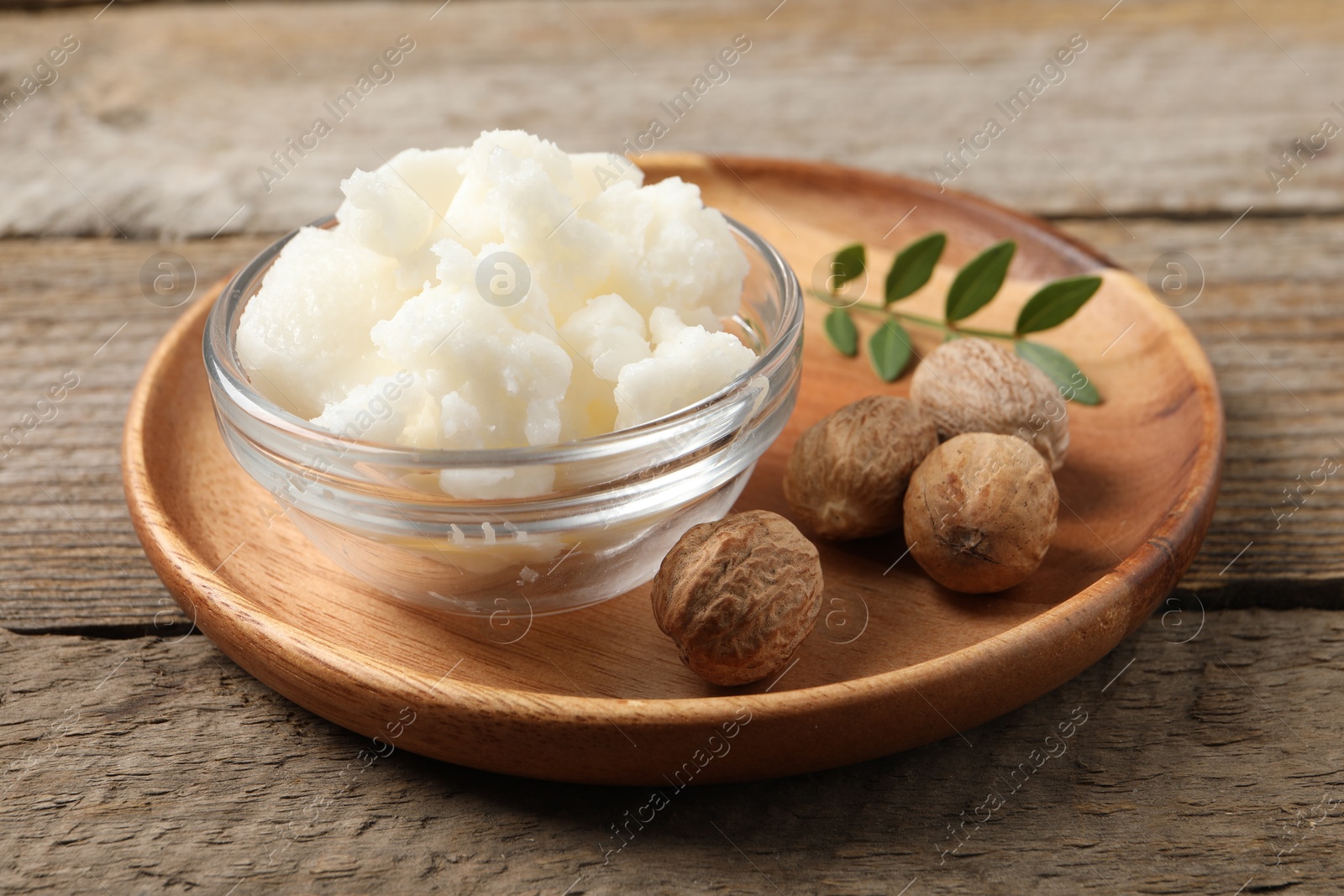 Photo of Shea butter in bowl and nuts on wooden table, closeup