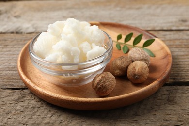 Photo of Shea butter in bowl and nuts on wooden table, closeup