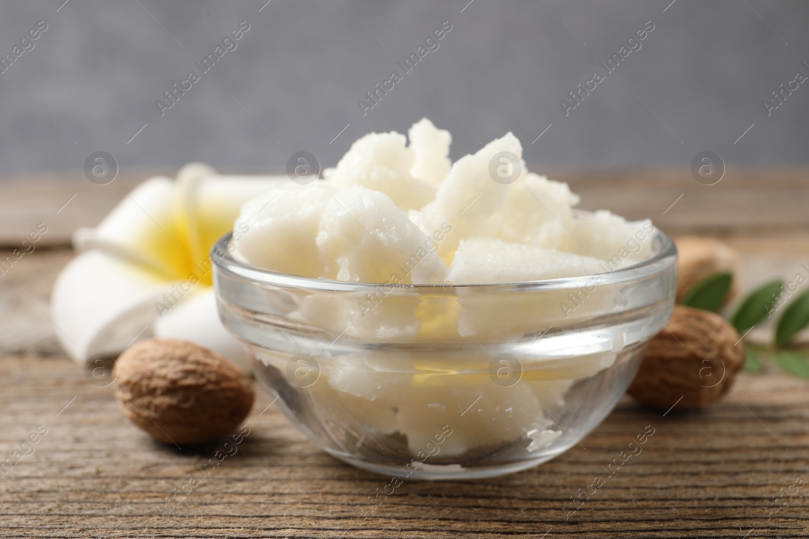 Photo of Shea butter in bowl, flower and nuts on wooden table, closeup