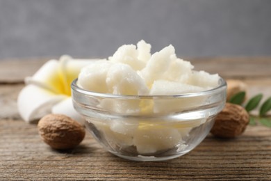 Shea butter in bowl, flower and nuts on wooden table, closeup