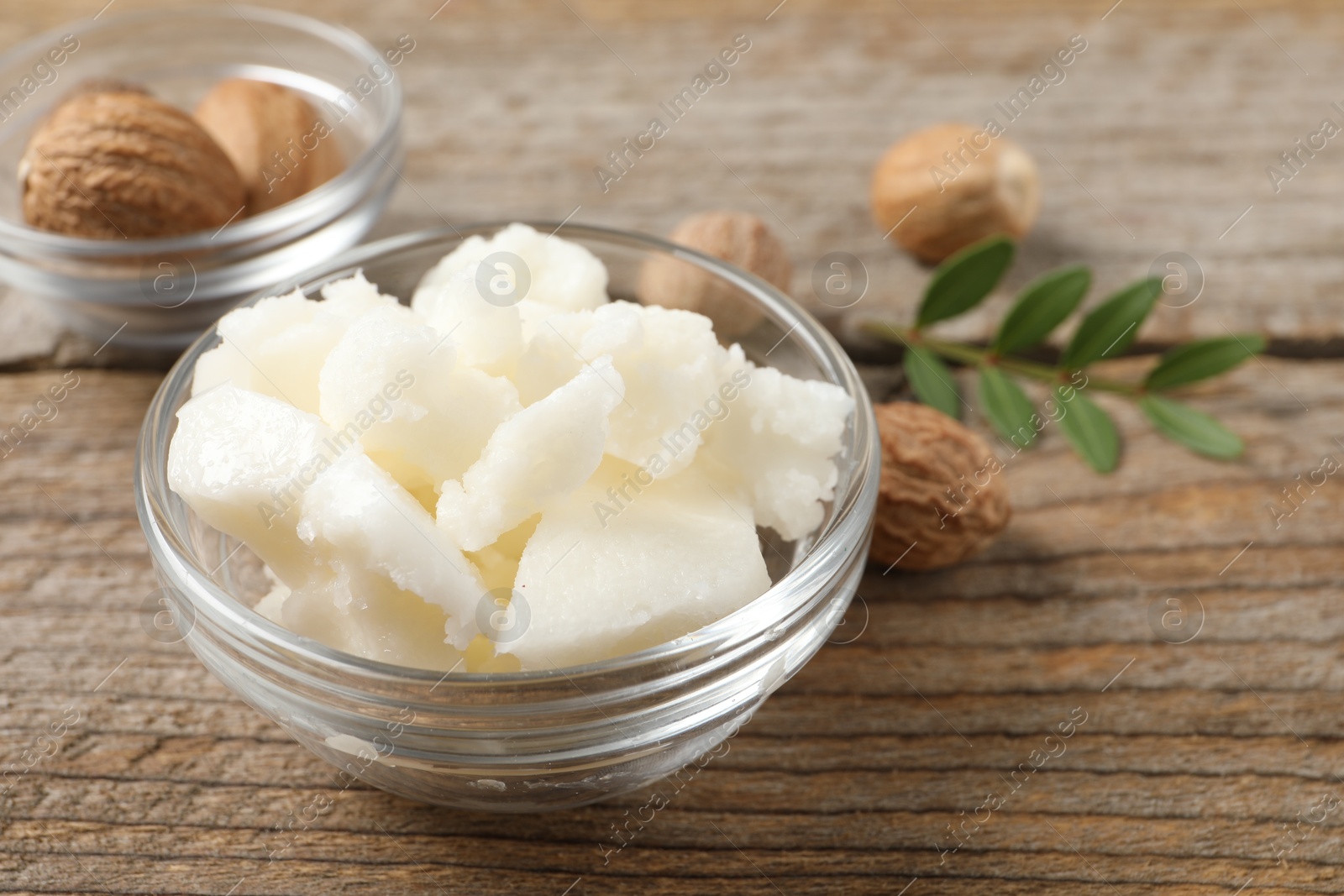 Photo of Shea butter in bowl and nuts on wooden table, closeup