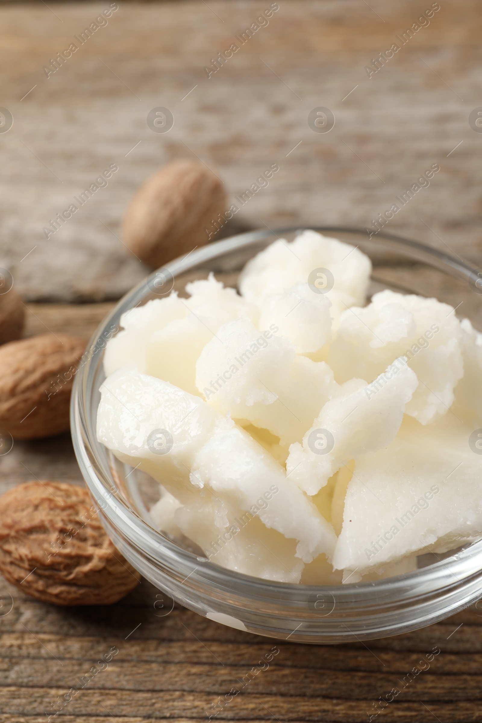 Photo of Shea butter in bowl and nuts on wooden table, closeup