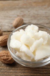 Shea butter in bowl and nuts on wooden table, closeup