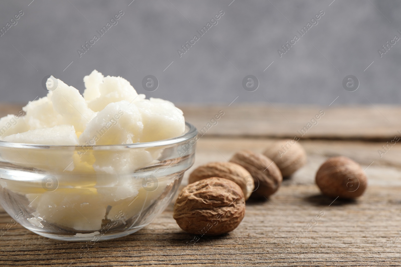 Photo of Shea butter in bowl and nuts on wooden table, closeup. Space for text