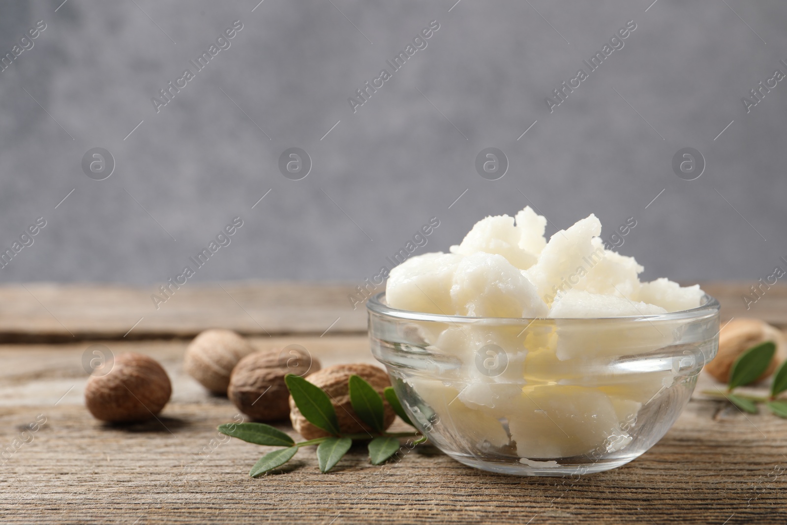 Photo of Shea butter in bowl and nuts on wooden table, closeup