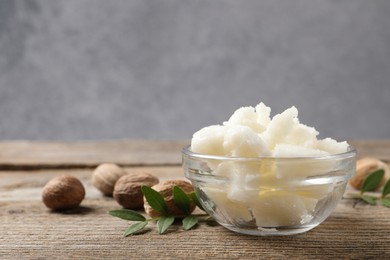 Photo of Shea butter in bowl and nuts on wooden table, closeup