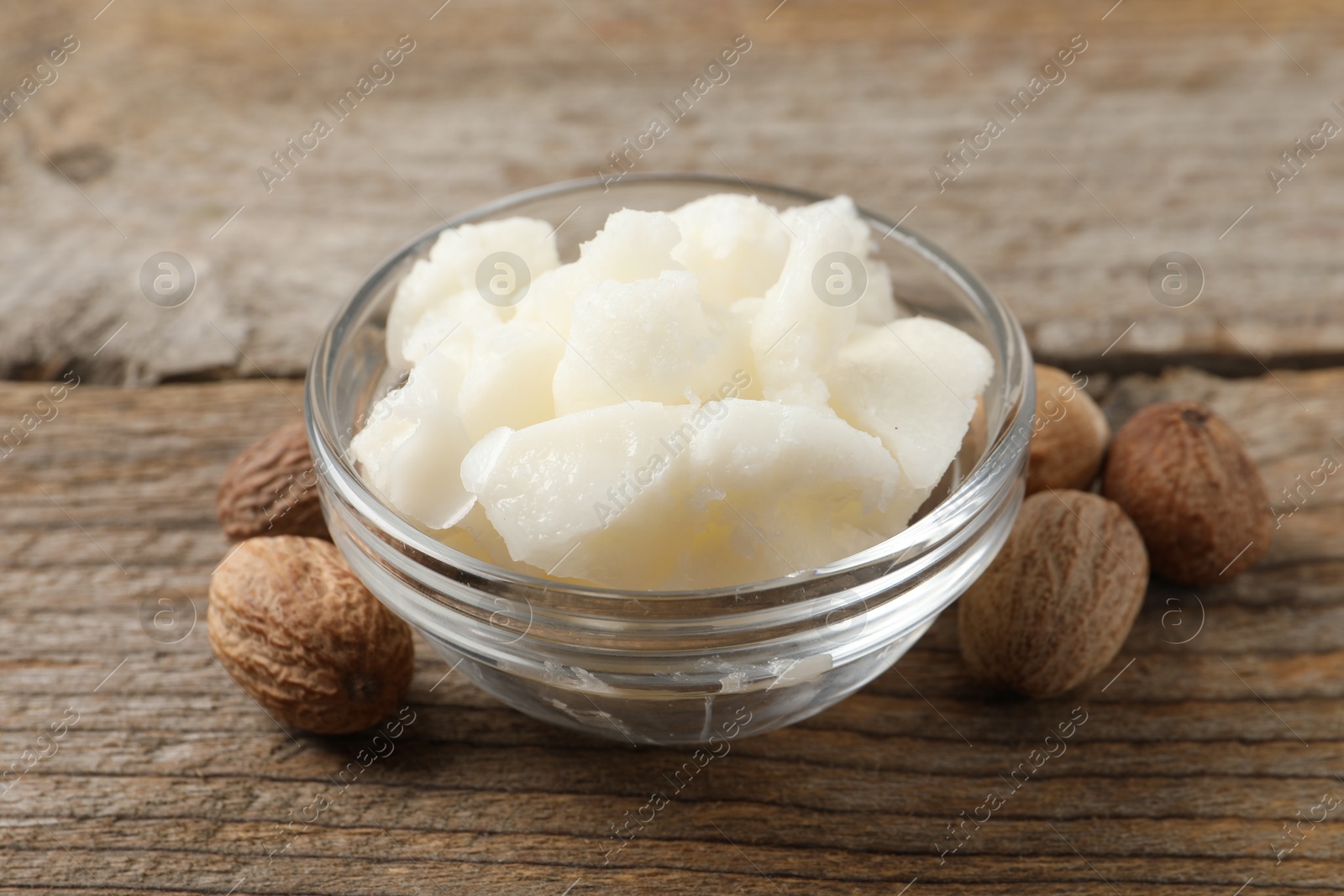 Photo of Shea butter in bowl and nuts on wooden table, closeup