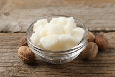 Shea butter in bowl and nuts on wooden table, closeup